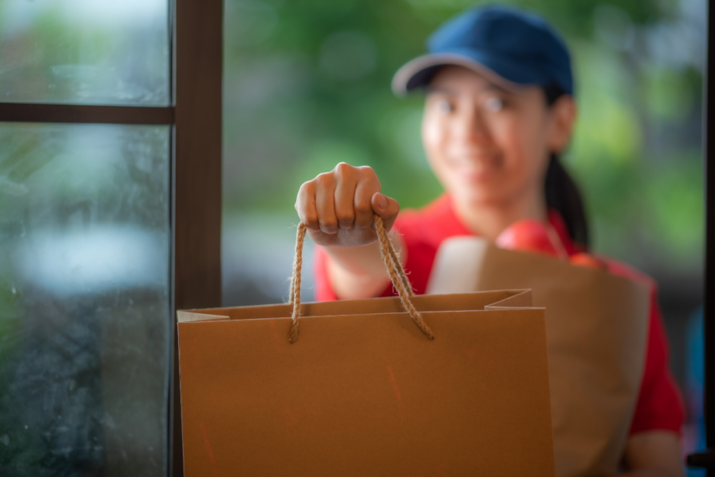 Delivery person in a red shirt holding paper shopping bags at a doorway