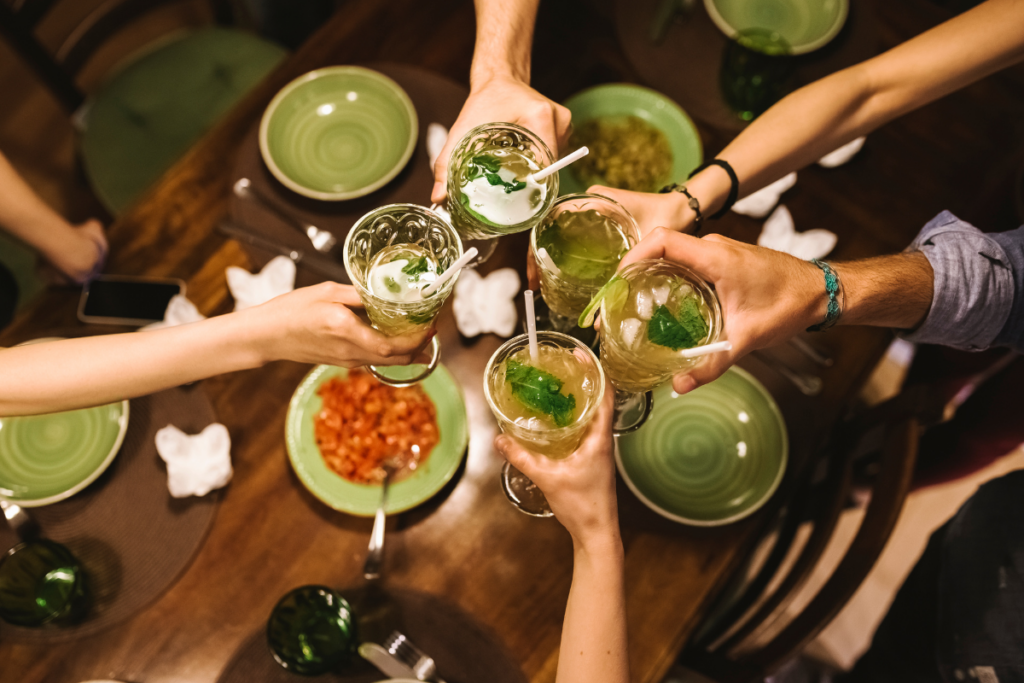 Friends raise glasses with mixed drinks over a dining table