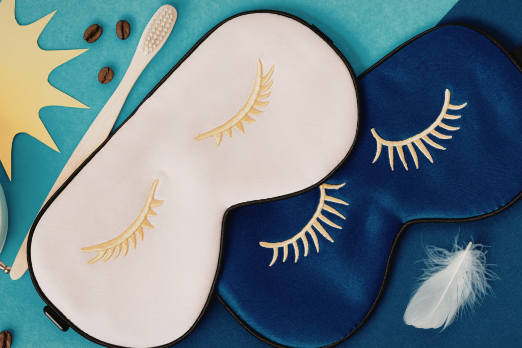 White and blue sleep masks beside a toothbrush, coffee beans, and a feather