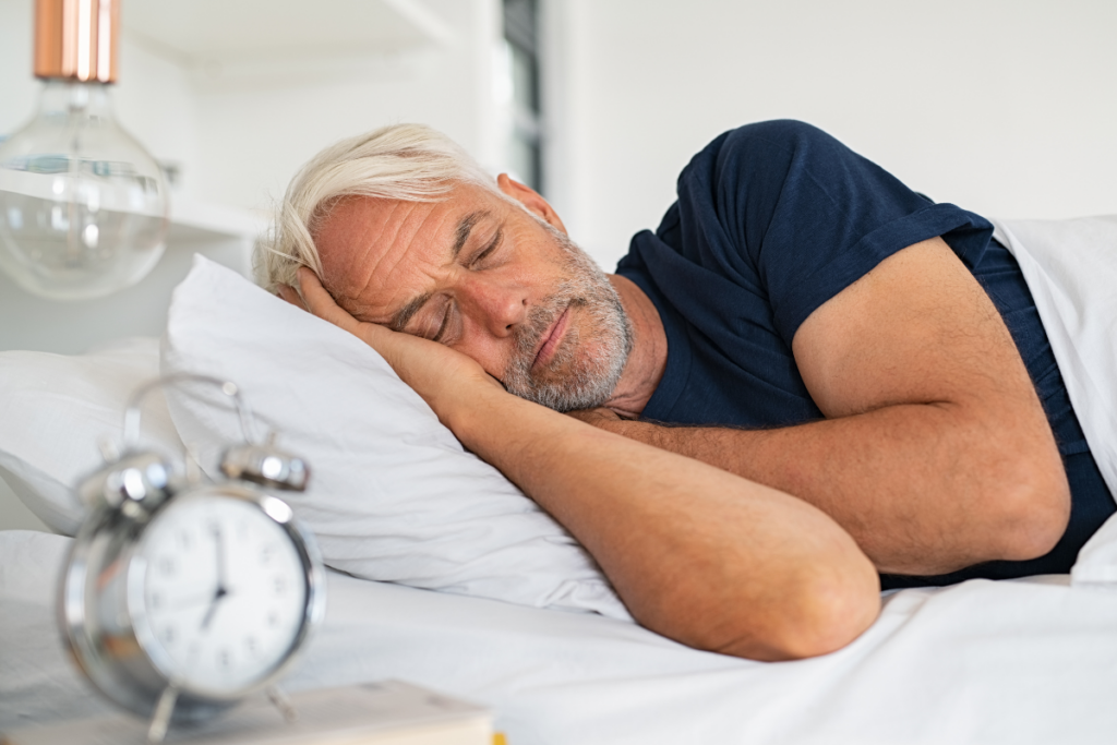 Older man sleeping on his side beside an alarm clock