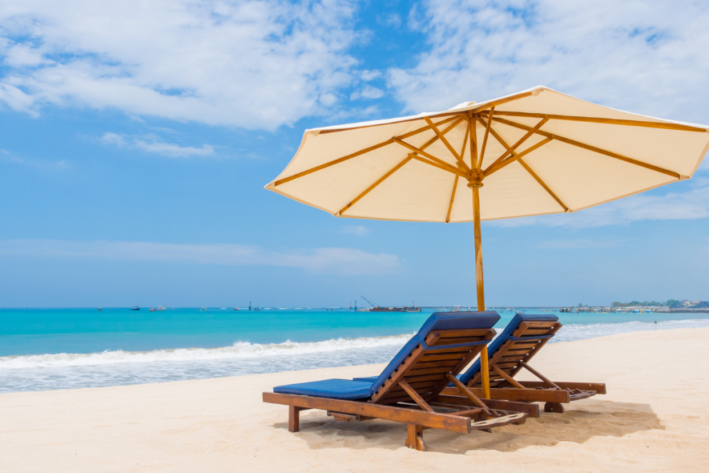 Two lounge chairs under a beach umbrella facing the ocean on a sunny day